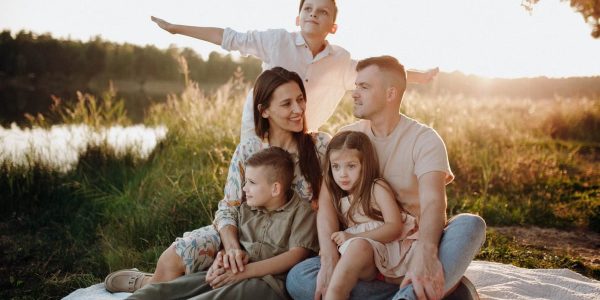 A family of five enjoying a serene picnic in a sunlit meadow during sunset.